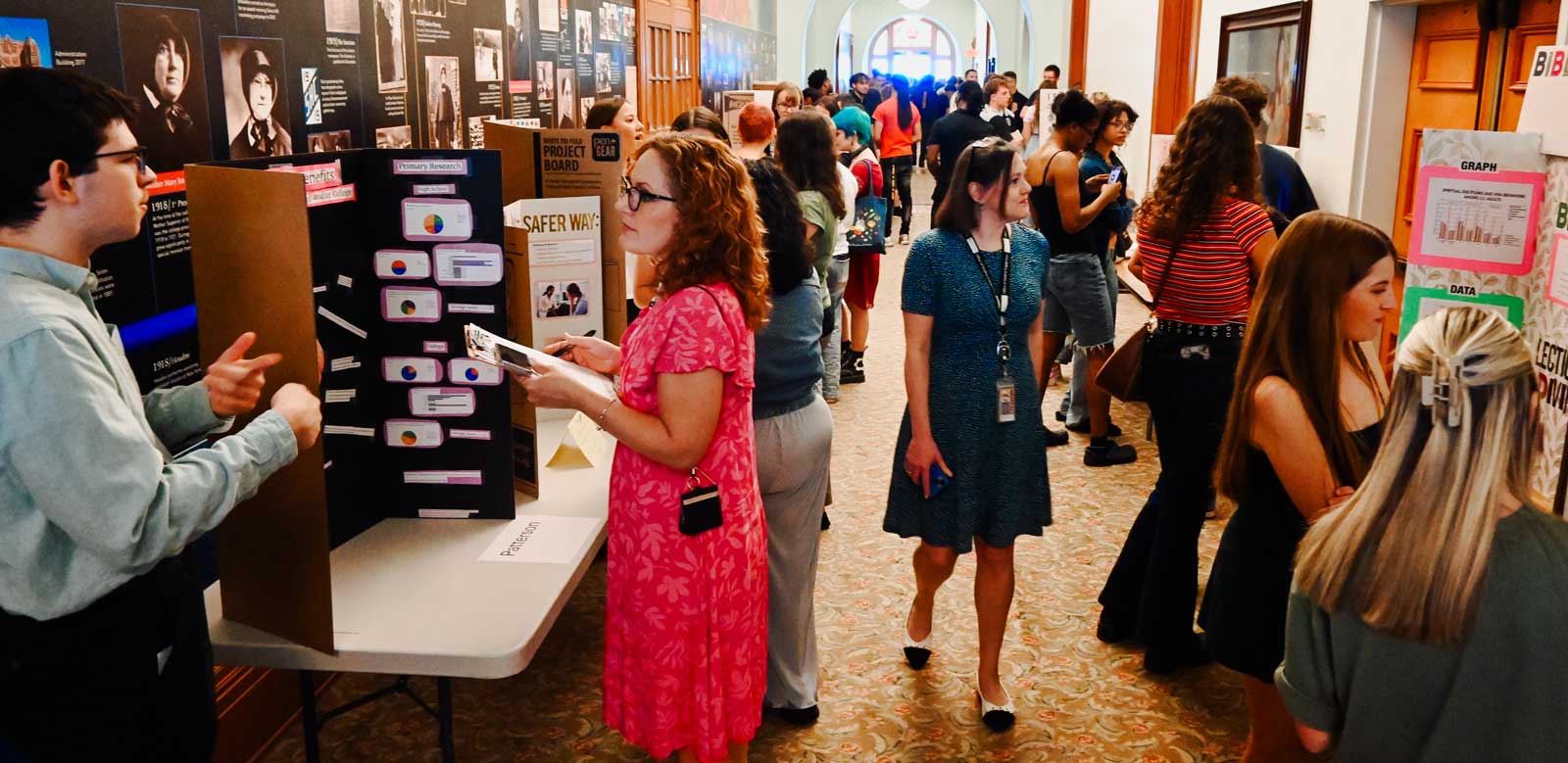 Many students and faculty in long hallway with presentations